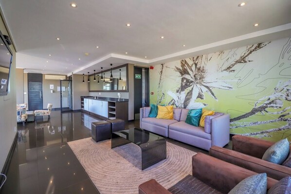 A modern lobby with a sofa, a coffee table, and a rug. There is a kitchen area in the background.