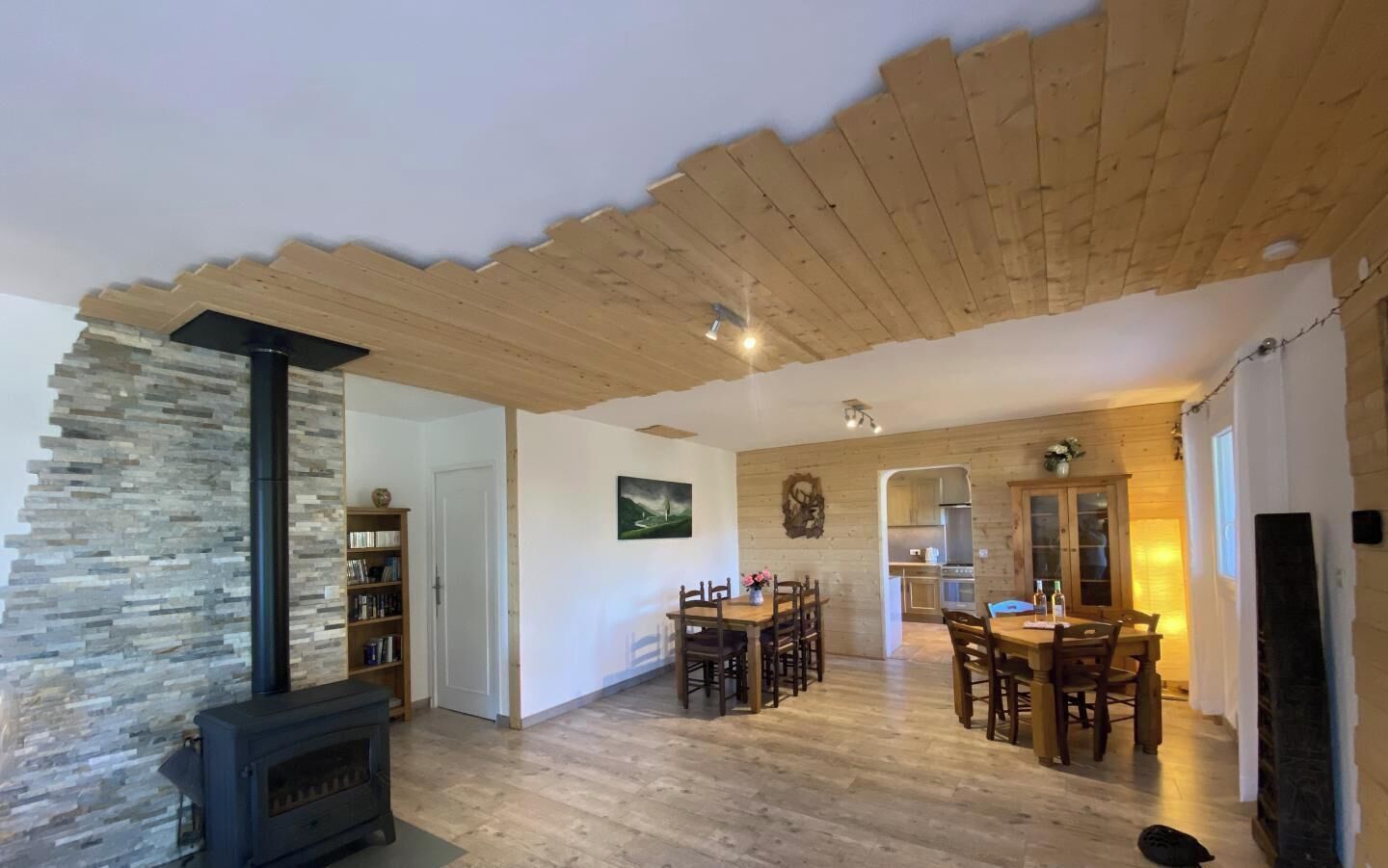 Una sala de estar acogedora con chimenea de piedra, techo de madera y comedor con mesa y sillas de madera.