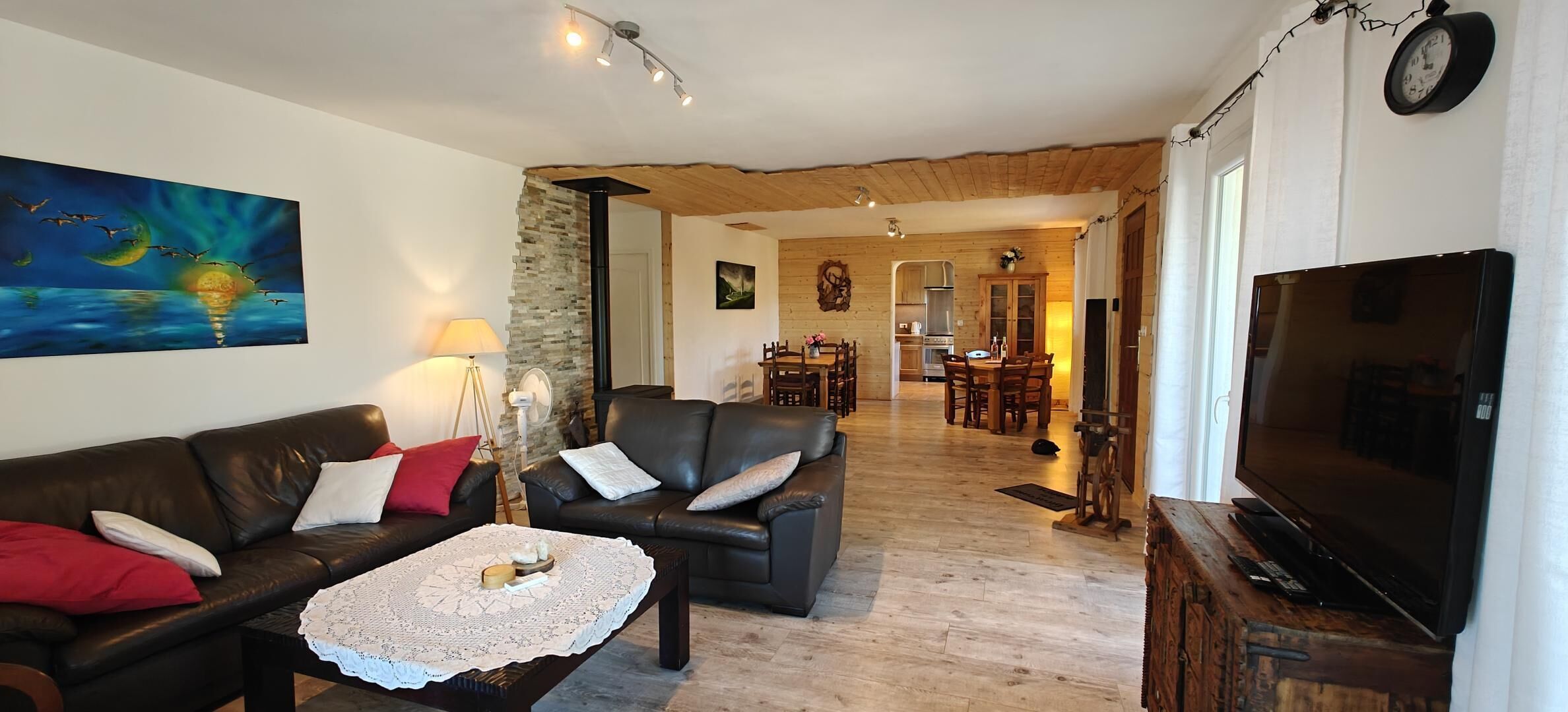 Una sala de estar acogedora con un sofá de cuero, una mesa de centro y un televisor. Se observa un comedor al fondo con una mesa y sillas.