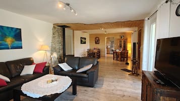 Una sala de estar acogedora con un sofá de cuero, una mesa de centro y un televisor. Se observa un comedor al fondo con una mesa y sillas.