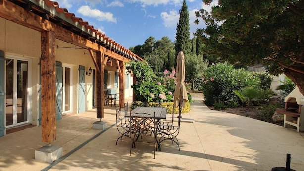 Ein überdachter Patio-Bereich mit Tisch und Stühlen, Holzbalken und einer Pergola.