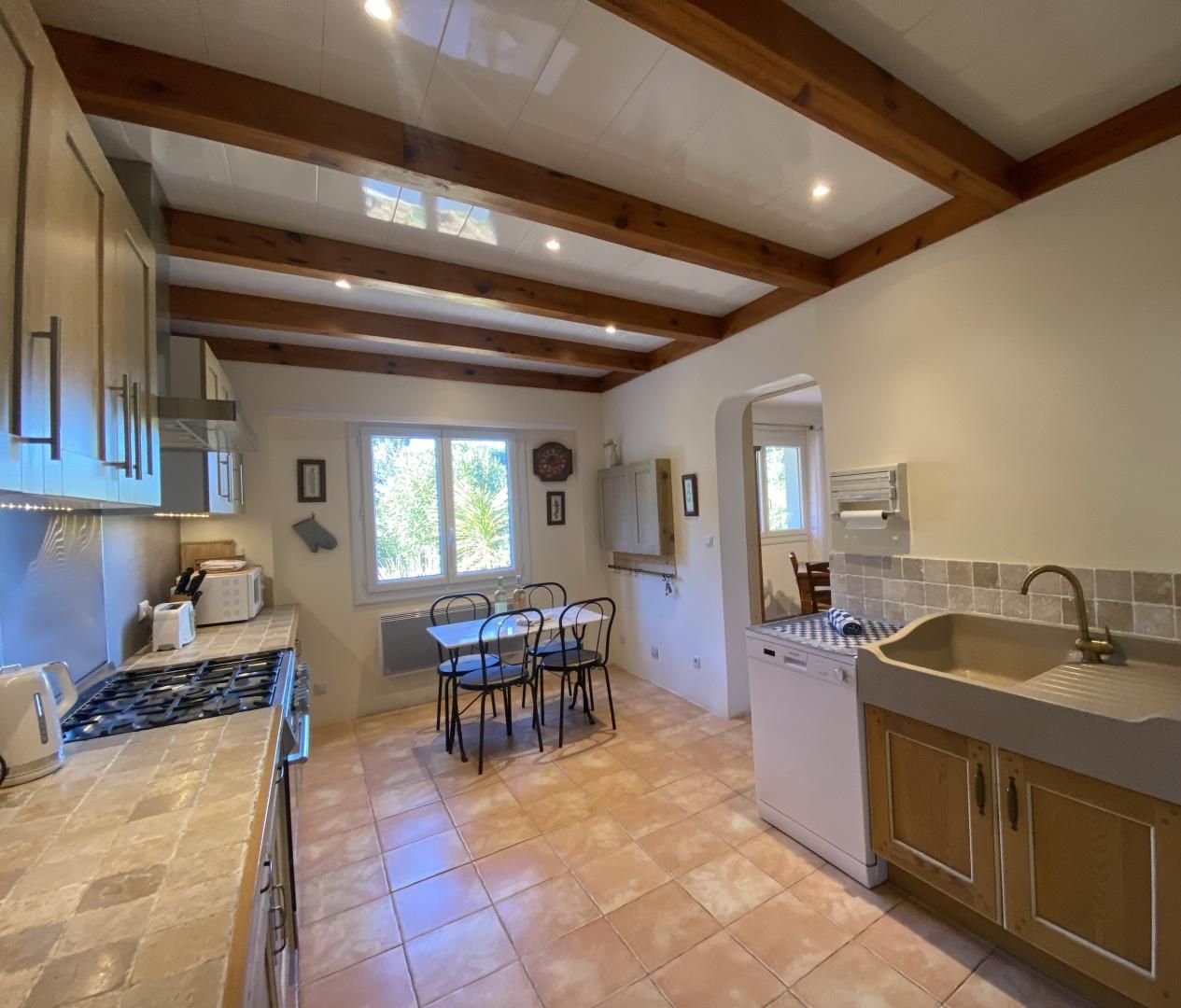 A kitchen with a stone tile floor, wooden beams, a sink, and a stove.