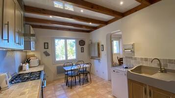 A kitchen with a stone tile floor, wooden beams, a sink, and a stove.