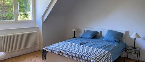 A bedroom with a bed, two bedside tables, a window, and a radiator.
