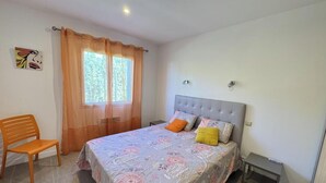 Ein Schlafzimmer mit einem Bett, einem Sessel, einem Fenster mit Vorhängen und einer Wandleuchte.