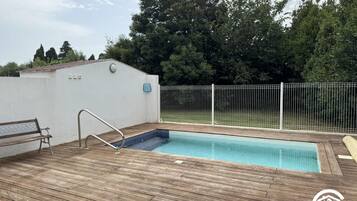 Une terrasse en bois avec une piscine, un banc et un mur blanc avec une porte.