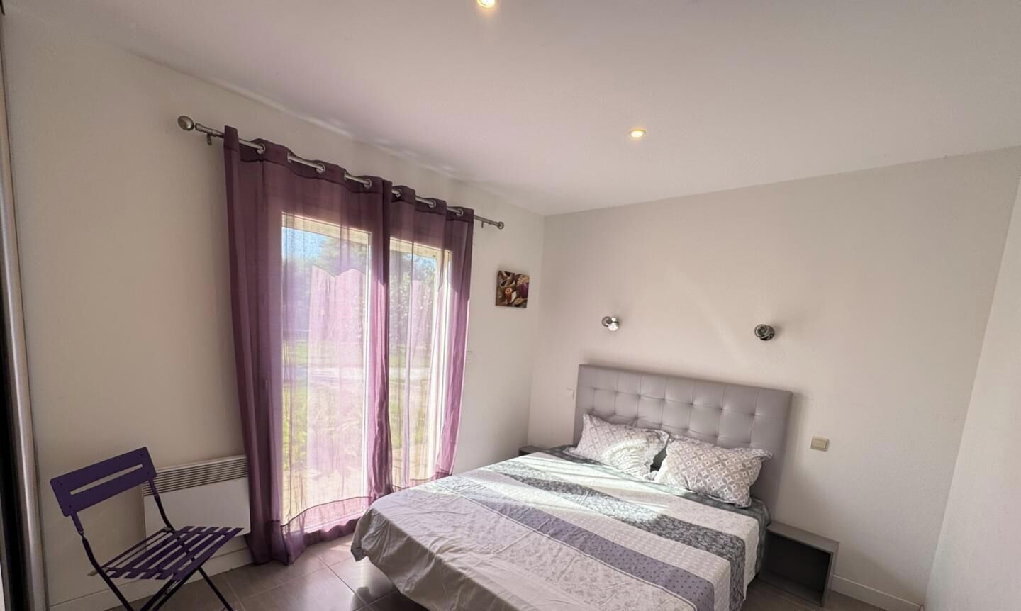 Un dormitorio con cama, una silla y un ventanal con cortinas.