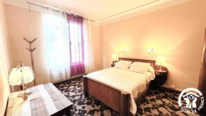 A hotel room with a bed, bedside lamps, a nightstand, a table with a lamp, and a window with curtains. - Le Clos de la Tour - CARCASSONNE (CARCASSONNE)