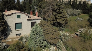 A stone building with a small window and a door, surrounded by trees and a castle in the background. - Le Clos de la Tour - CARCASSONNE (CARCASSONNE)