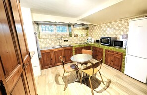 A compact kitchen with wooden cabinets, a round table, and a white refrigerator.