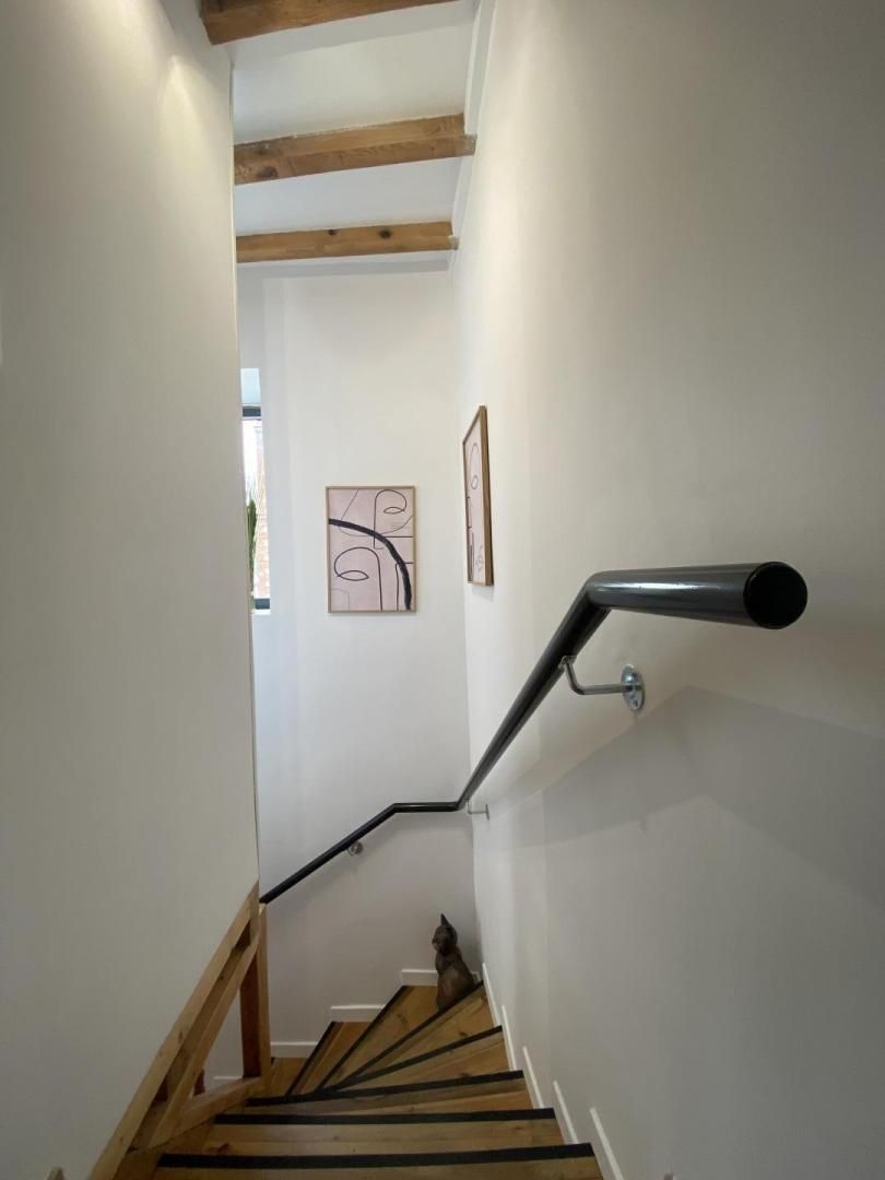 Una escalera de madera con barandilla, paredes blancas y una obra de arte abstracta enmarcada en la pared.