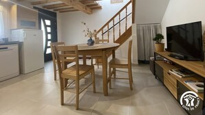 A cozy kitchen with wooden beams, a dining table with chairs, a TV, and a staircase leading to another room. - Nicou's house - CLARA-VILLERACH (CLARA-VILLERACH)