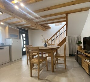 A cozy kitchen with wooden beams, a dining table with chairs, a TV, and a staircase leading to another room.