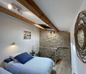A bedroom with a bed, a stone wall, a wooden ceiling, and a painting.