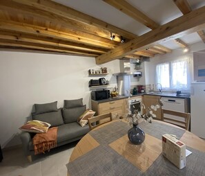 A cozy living room with a sofa, a coffee table with a vase, and a kitchen area with a microwave, kettle, and refrigerator.