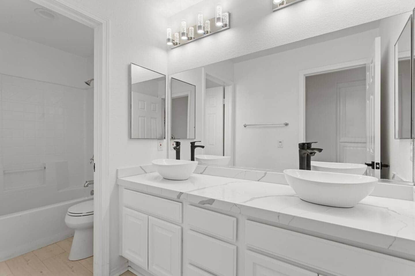 A modern bathroom with a white vanity, two sinks, a large mirror, and a shower area.