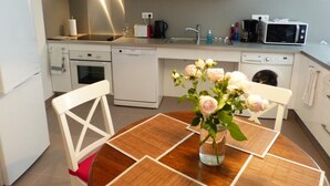 Eine moderne Küche mit weißen Schränken, einer Mikrowelle, einem Toaster und einem Spülbecken. Auf dem Esstisch steht eine Vase mit Blumen.