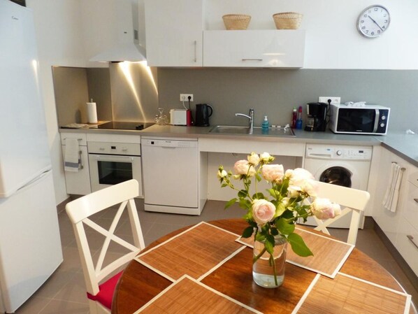 Una cocina moderna con armarios blancos, microondas, tostadora y fregadero. Hay un jarrón con flores sobre la mesa de comedor.