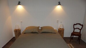 Ein Bett mit einer beigefarbenen Tagesdecke, zwei Nachttischlampen und einem Holzstuhl.