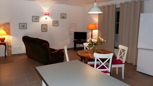 Ein kompakter Wohnbereich mit einer Couch, einem Esstisch mit Stühlen, einem Fernseher und einer kleinen Küchenzeile.