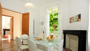 Ein Essbereich mit einem Glastisch, weißen Stühlen, einem Kamin und Blick auf Grün durch ein Fenster.