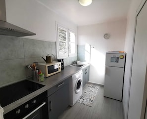 Una cocina compacta con microondas, hervidor, lavabo y lavadora.