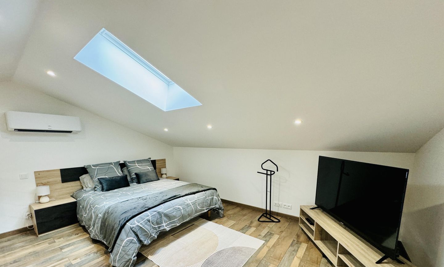 A bedroom with a skylight, a bed, a TV, and a wooden floor.