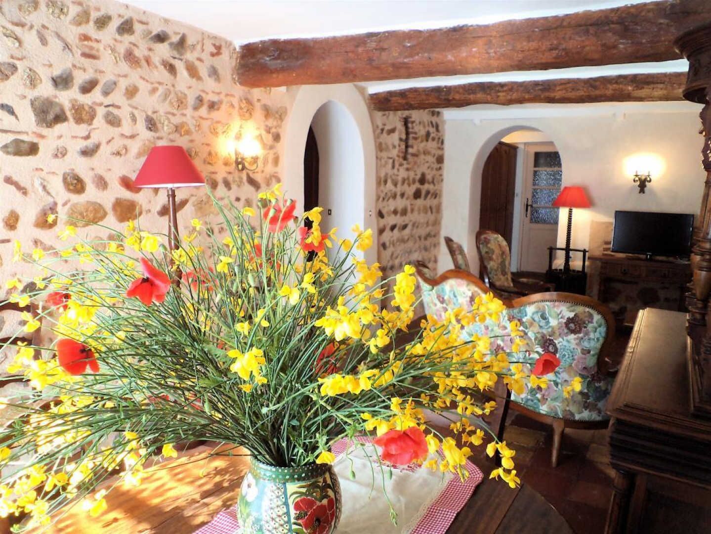 A rustic room with stone walls, a wooden ceiling, a floral vase on a table, a chair, and a television.