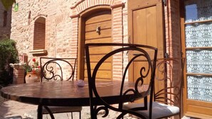 An outdoor patio with a round table and metal chairs, a stone wall, and a wooden door with a glass panel. - Dona Lucrècia - PONTEILLA (PONTEILLA)