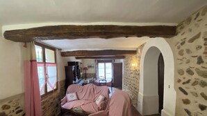 A cozy room with a stone wall, a wooden ceiling beam, a bed with a pink checkered bedspread, and a small table with a red chair. - Dona Lucrècia - PONTEILLA (PONTEILLA)