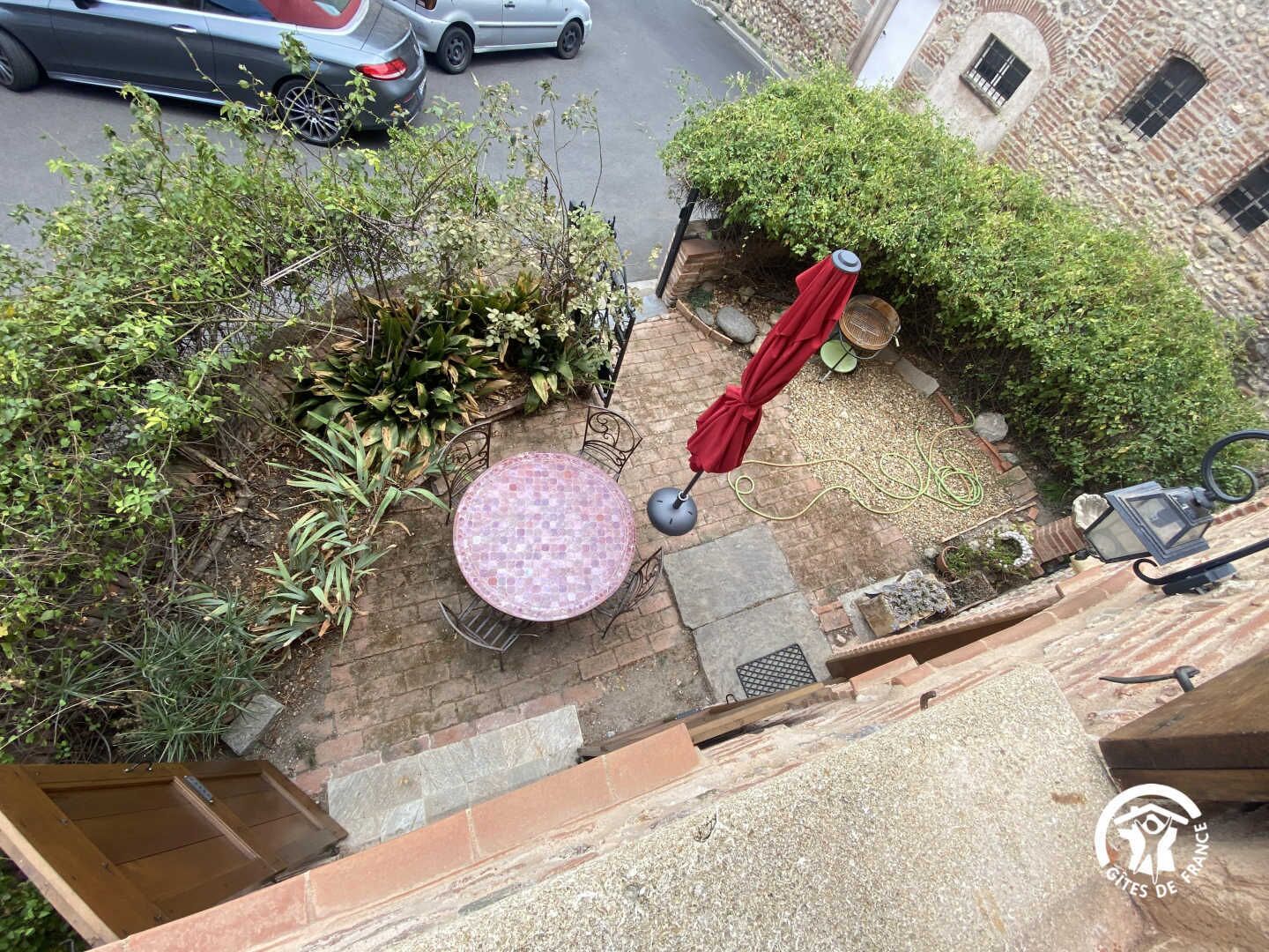 A patio area with a mosaic table, a red umbrella, and a stone wall.