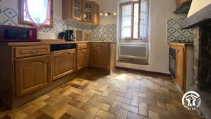 A kitchen with wooden cabinets, a microwave, a window with lace curtains, and a herringbone-patterned floor. - Dona Lucrècia - PONTEILLA (PONTEILLA)