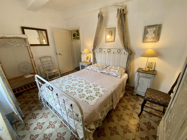 Un dormitori amb un llit amb cortines, una cadira, una taula de nit amb una làmpada i un mirall a la paret.