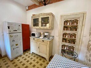 Una cuina compacta amb nevera, microones, cafetera i un armari amb portes de vidre.