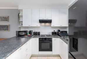 Une cuisine moderne avec des meubles blancs, une cuisinière noire, un four à micro-ondes et un réfrigérateur.