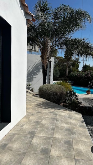 Un sendero pavimentado que conduce a una piscina rodeada de palmeras y un edificio blanco.