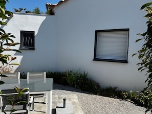 A white building with a patio area, a table with chairs, and a window with blinds.