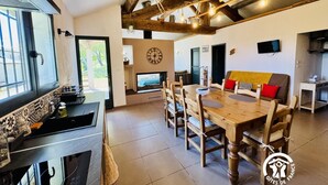 A cozy, rustic interior with exposed wooden beams, a wooden dining table, and a TV mounted on the wall. - Nore & Nature - PRADELLES CABARDES (PRADELLES CABARDES)