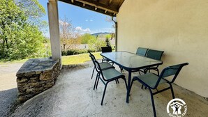 An outdoor patio with a table and chairs, a stone wall, and a view of trees and hills. - Nore & Nature - PRADELLES CABARDES (PRADELLES CABARDES)