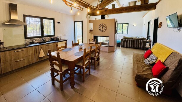 A spacious living area with a wooden dining table, a sofa with cushions, and a fireplace. - Nore & Nature - PRADELLES CABARDES (PRADELLES CABARDES)