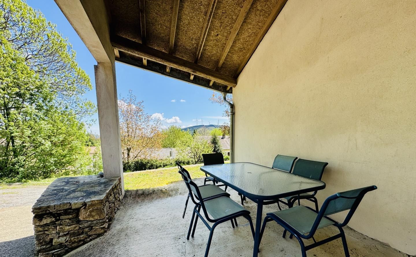 Un patio al aire libre con una mesa y sillas, un muro de piedra y vistas a árboles y colinas.