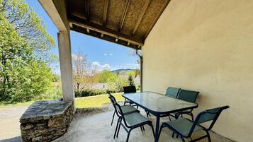 Un patio al aire libre con una mesa y sillas, un muro de piedra y vistas a árboles y colinas.
