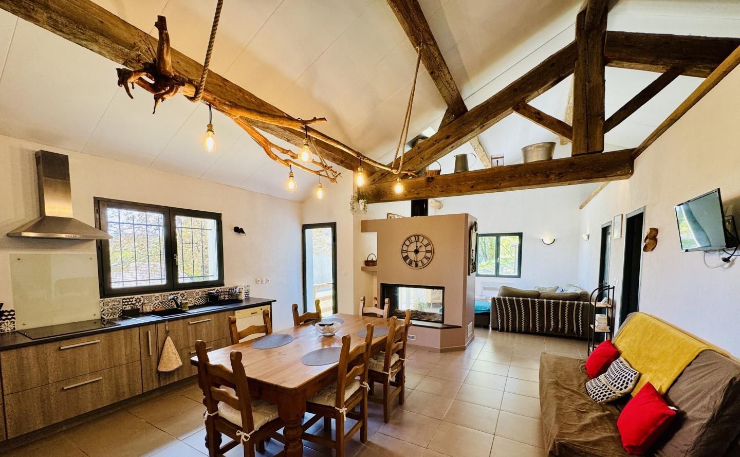 A spacious living area with a wooden dining table, a sofa with cushions, and a fireplace.