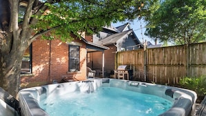 A backyard with a hot tub, a brick house, a wooden fence, and a grill. - *NEW* Walk 2 Short North | Hot Tub | Easy Parking (Columbus)
