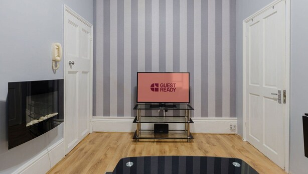 Una habitación con papel tapiz a rayas, un televisor sobre un pedestal de vidrio, una chimenea y dos puertas.