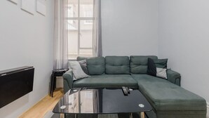 Una sala de estar moderna con un sofá modular, un televisor de pantalla plana, una mesa de centro y una ventana con cortinas.