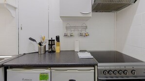 Una cocina con estufa, microondas y pileta. Hay utensilios y un rollo de toallas de papel sobre la encimera.
