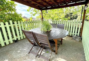 An outdoor patio with a round wooden table and chairs, surrounded by a white picket fence. - Chai du Canal - SALLELES D'AUDE (SALLELES D AUDE)
