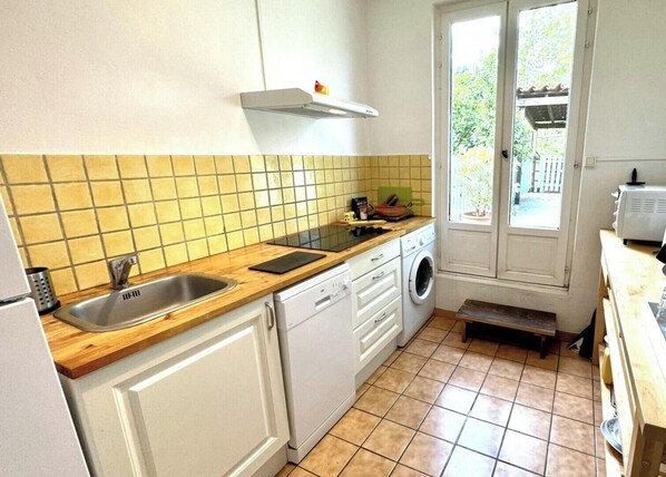 Une cuisine compacte équipée d’un évier, d’un lave-linge et d’une fenêtre donnant sur un jardin.