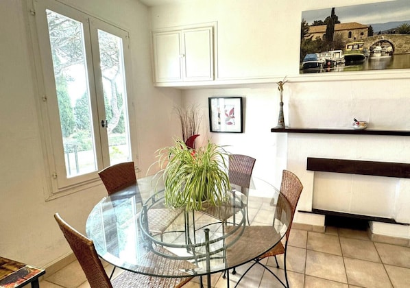 A dining area with a glass table, wicker chairs, and a potted plant. - Chai du Canal - SALLELES D'AUDE (SALLELES D AUDE)